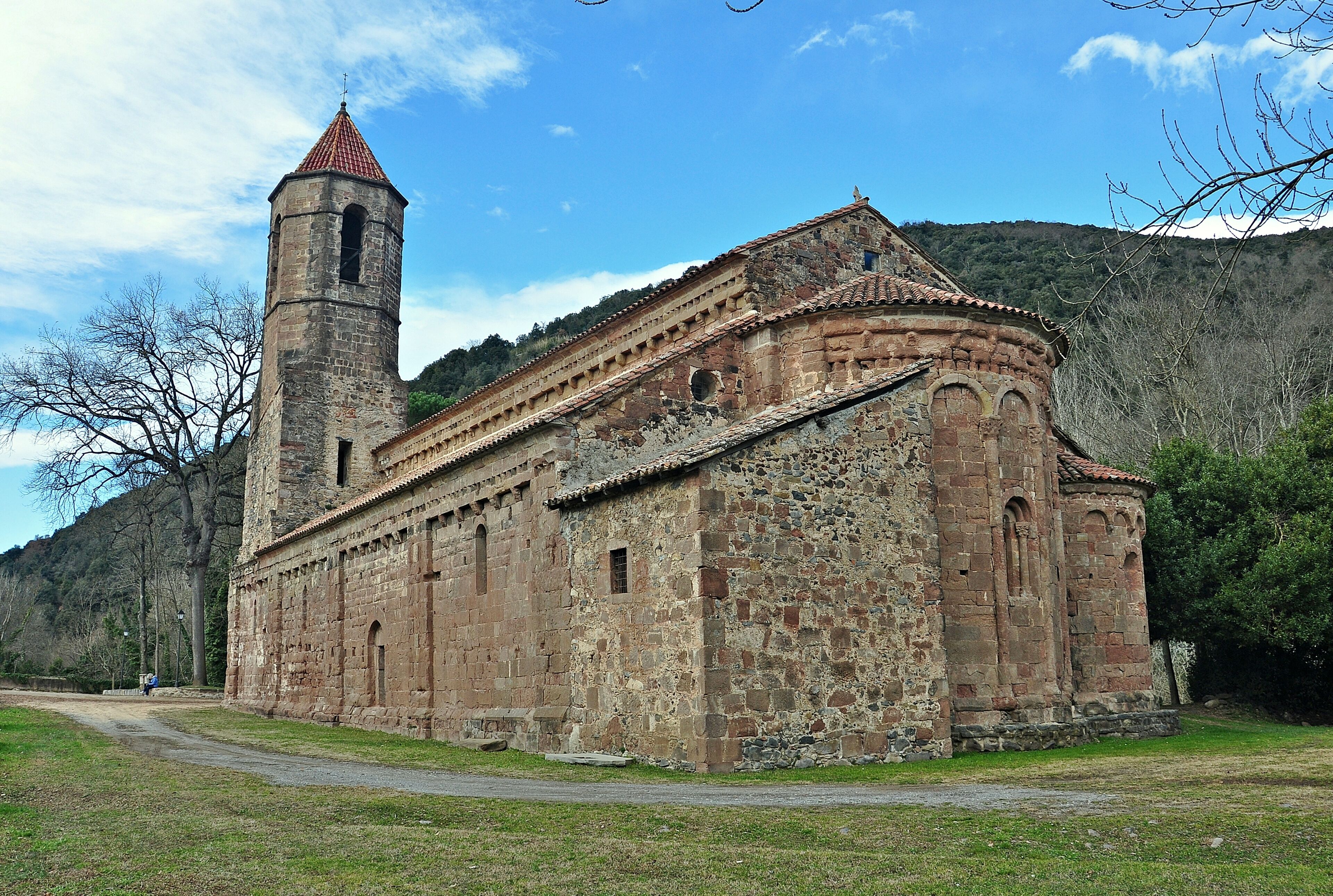 A historic stone church with a bell tower, surrounded by a grassy area and hills in the background.