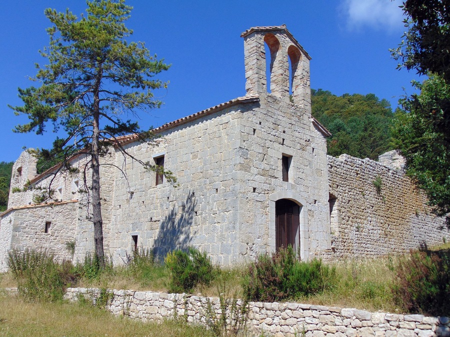 An old stone building with a bell tower, surrounded by trees and grass.