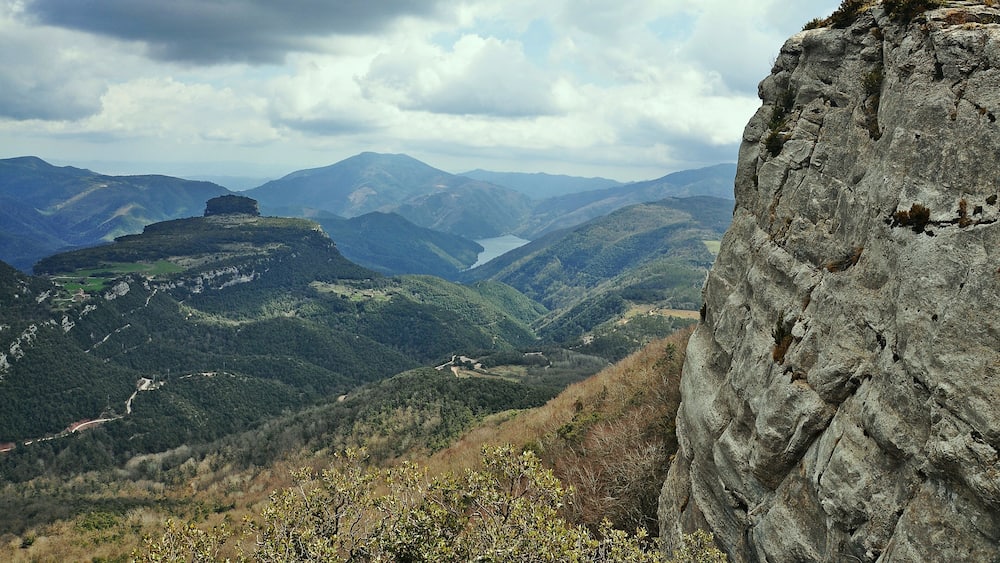 A mountainous landscape with a prominent rock formation and a valley with a lake.