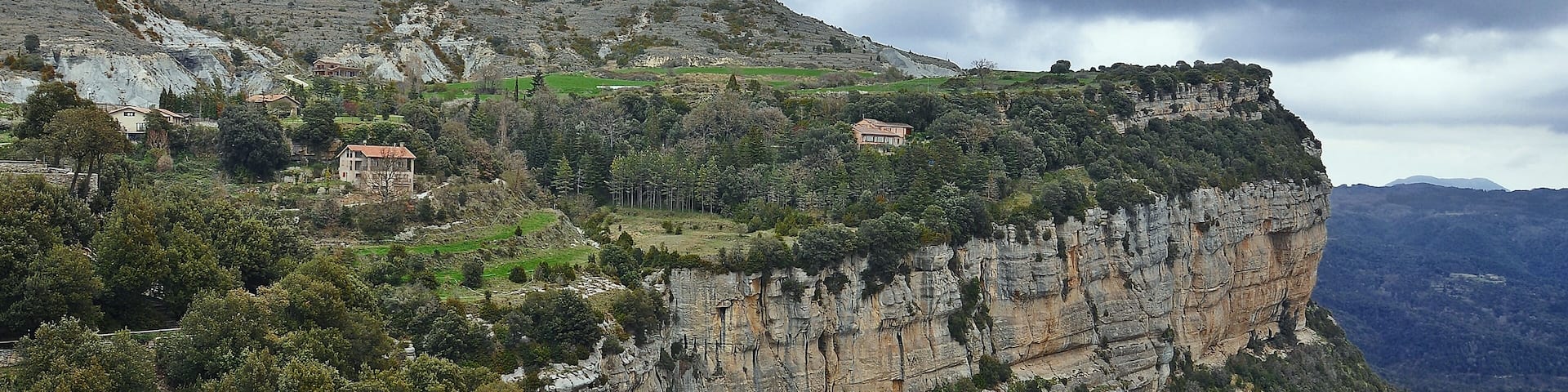 A mountainous landscape with houses perched on the cliff edge and dense forested areas.