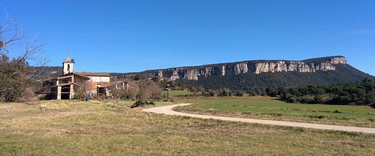 A rural landscape with a church, a dirt path, and a mountain in the background.