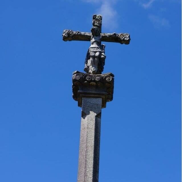 A stone cross with a figure of Jesus Christ, set against a clear blue sky.