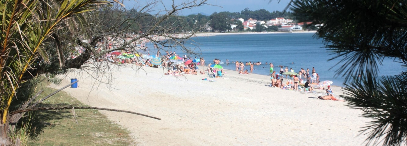 Una playa con gente tomando el sol y nadando, rodeada de palmeras y un cielo azul despejado.