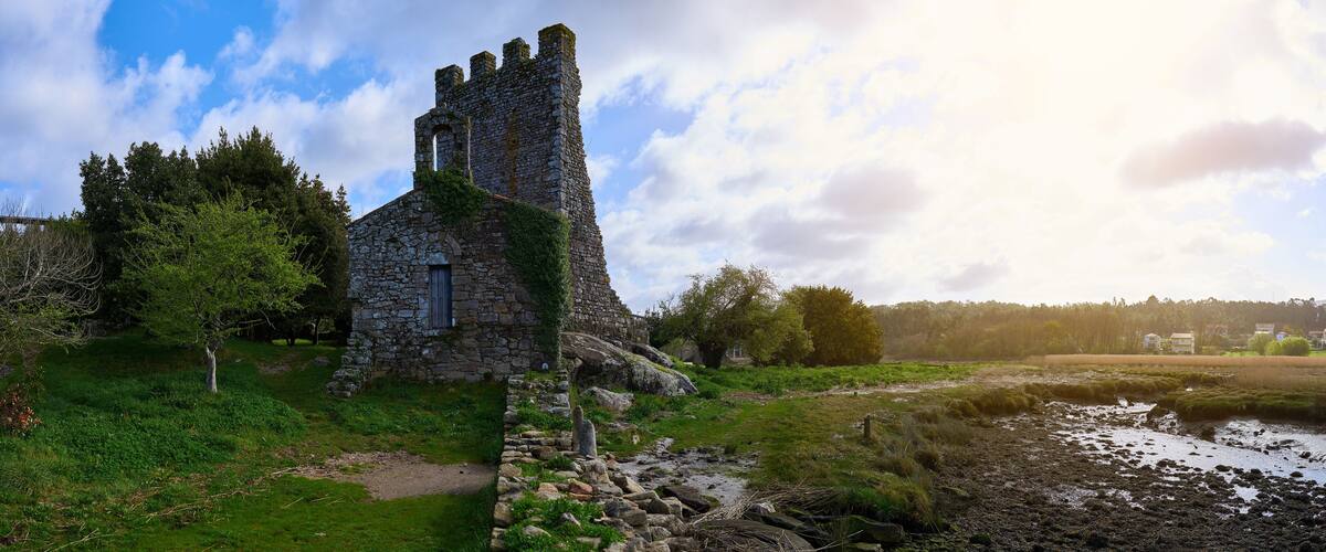 A stone church with a tower, surrounded by trees and a grassy field.
