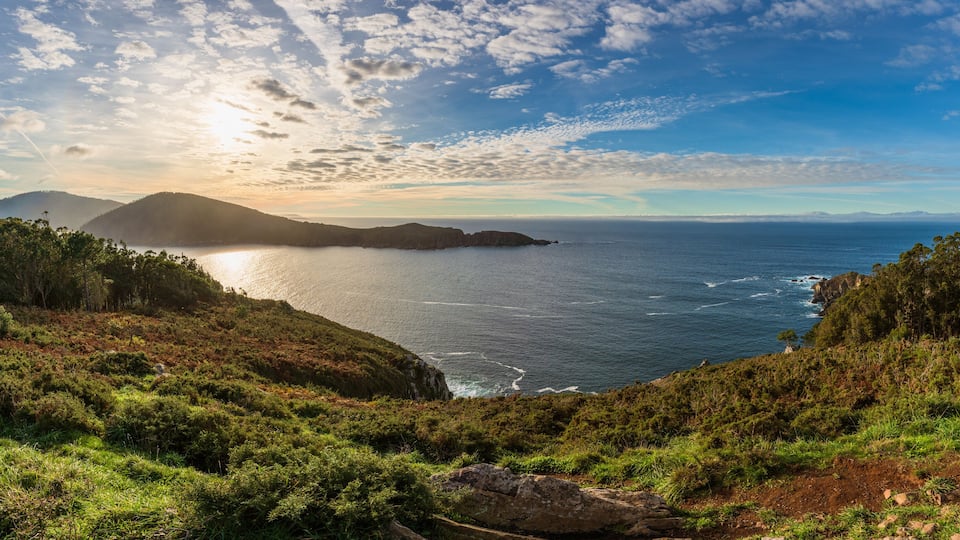A coastal landscape with a view of the ocean, hills, and a clear sky.