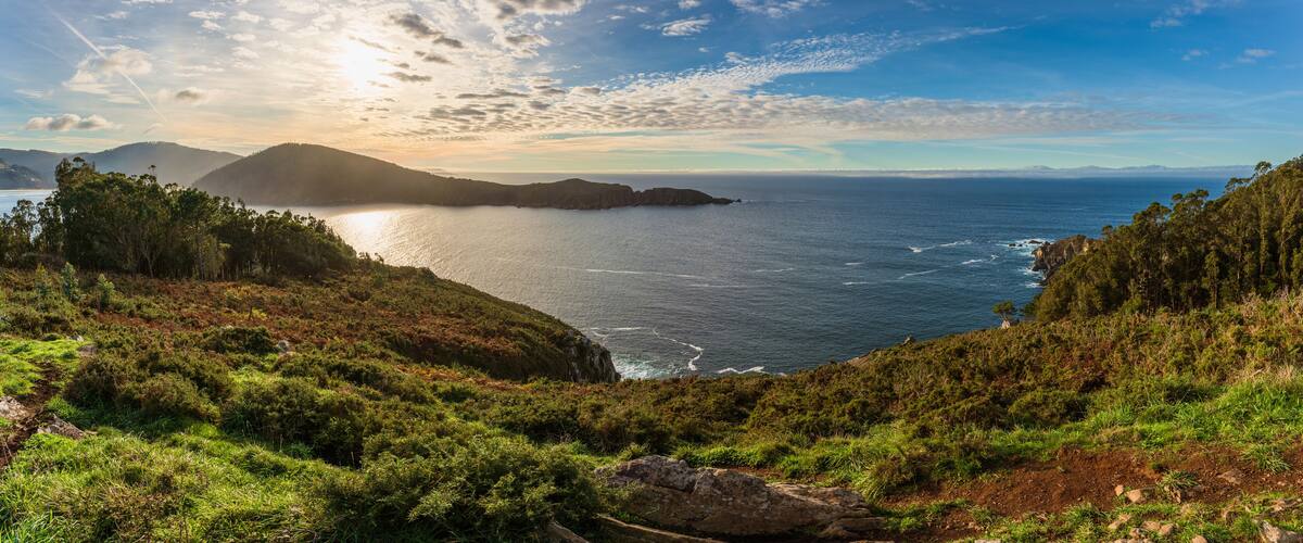 A coastal landscape with a view of the ocean, hills, and a clear sky.