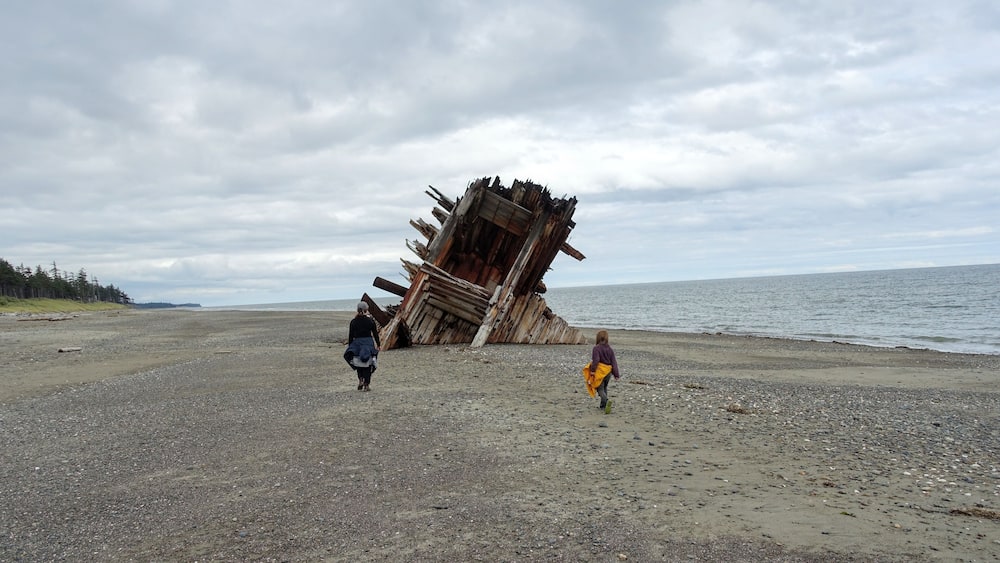 A mom and daughter exploring the Pesuta Shipwreck site, a popular tourist attraction outside Tlell, in Naikoon Provincial Park, Haida Gwaii, Canada. The wooden ship is on a sandy beach by the ocean