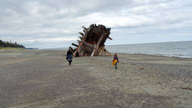 A mom and daughter exploring the Pesuta Shipwreck site, a popular tourist attraction outside Tlell, in Naikoon Provincial Park, Haida Gwaii, Canada. The wooden ship is on a sandy beach by the ocean