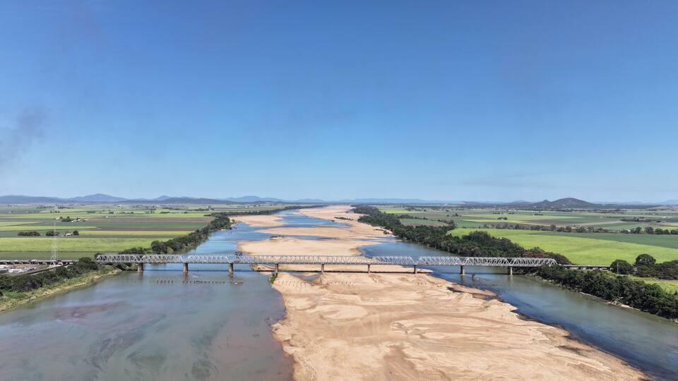 A river flowing under a bridge with green fields and distant hills.