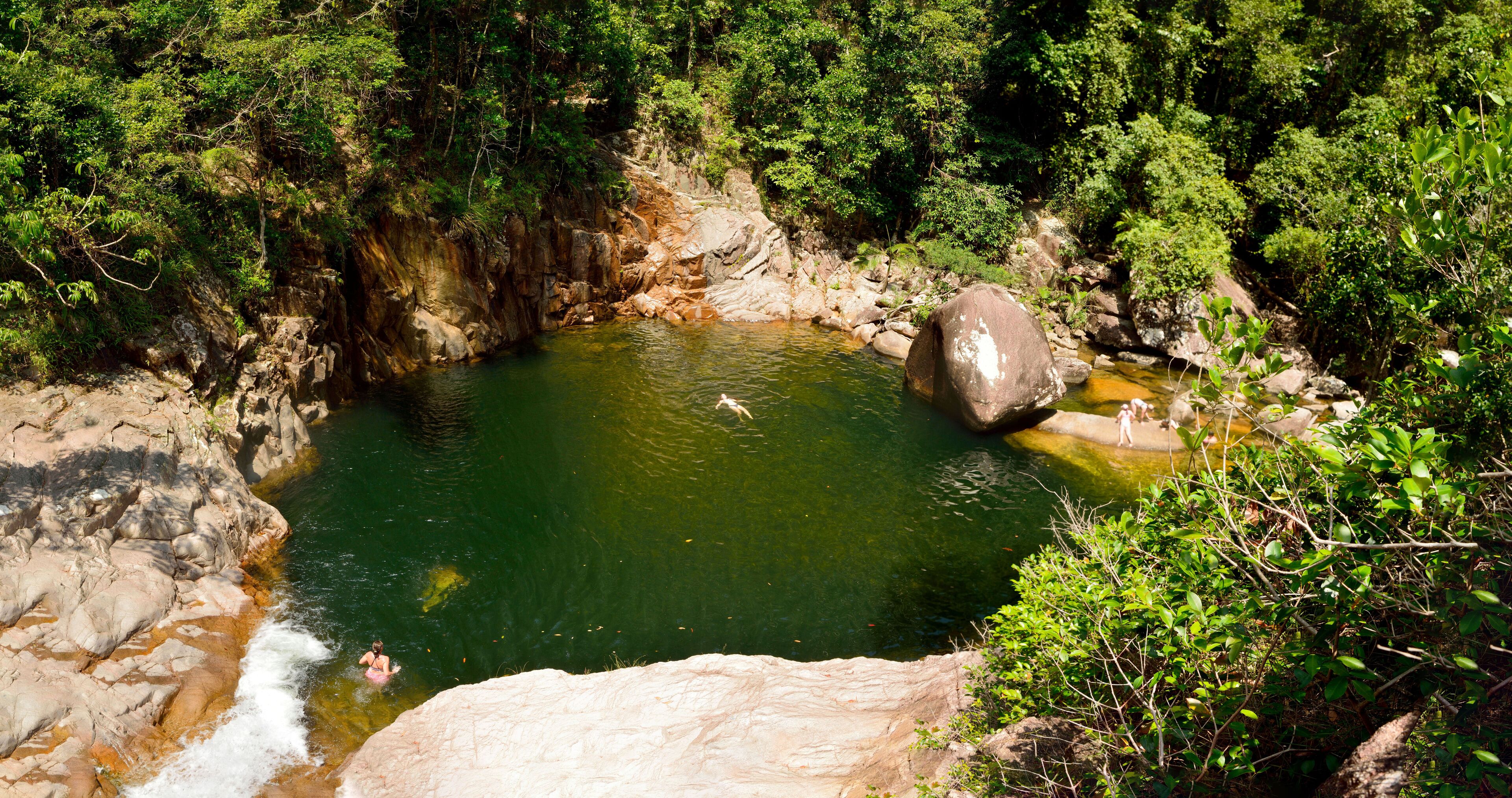A natural pool surrounded by rocky terrain and dense forest.
