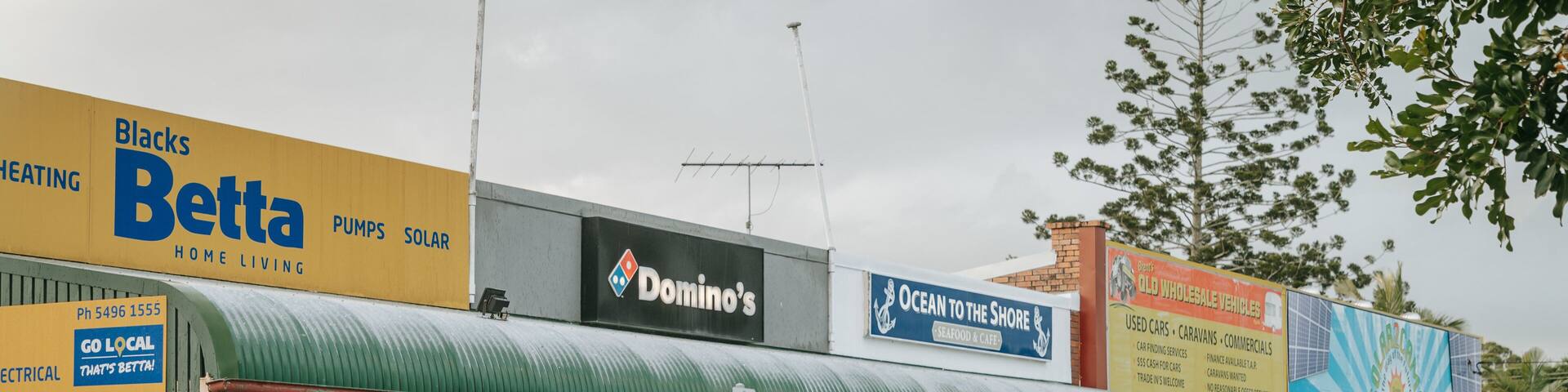 A street with various shops including a Domino's, a seafood restaurant, and a solar panel store.