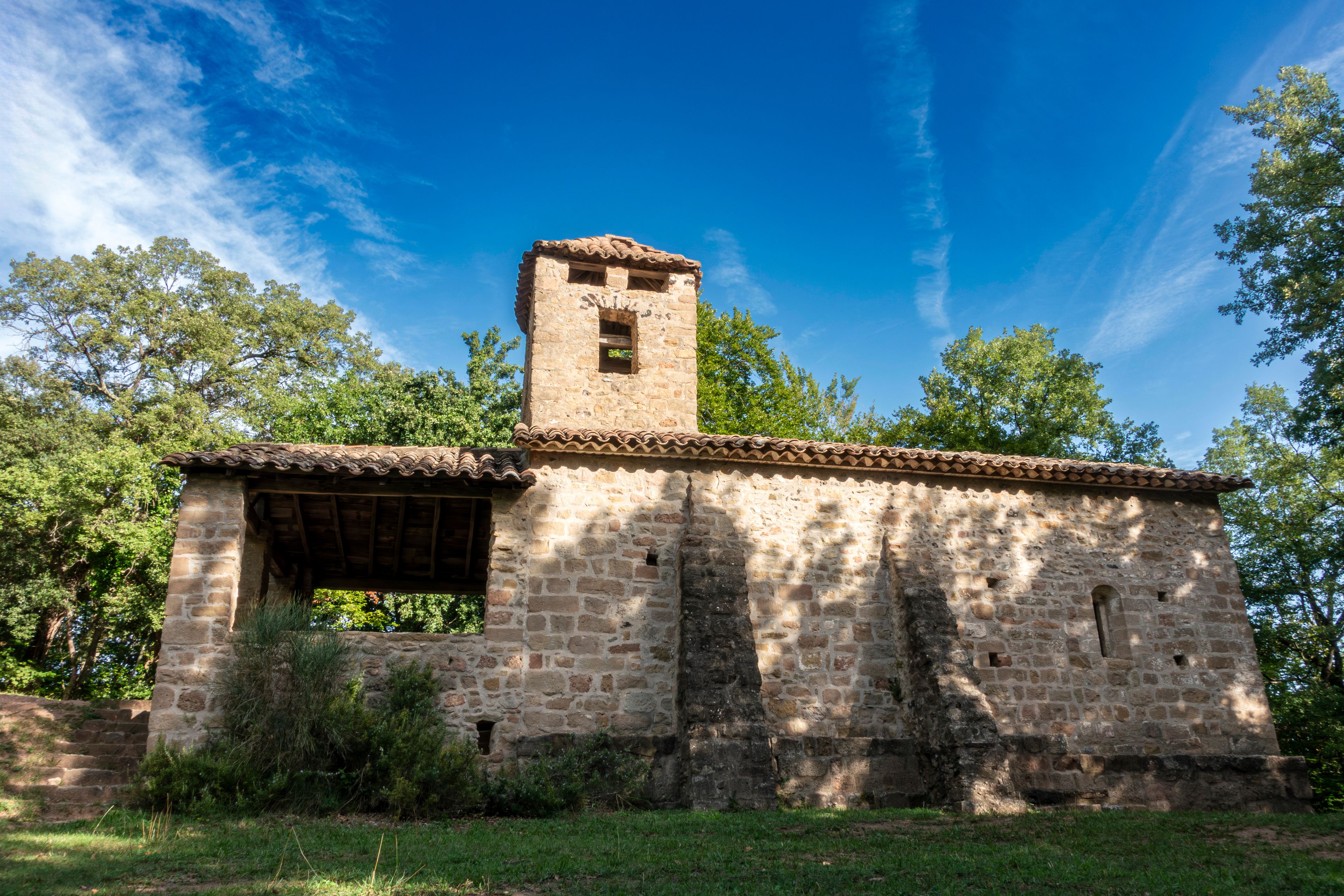 Una iglesia de piedra con un campanario, rodeada de árboles y césped.