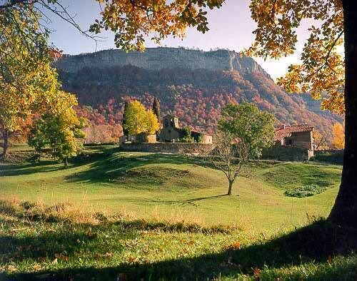 A rural landscape with rolling hills, a small house, and trees with autumn foliage.