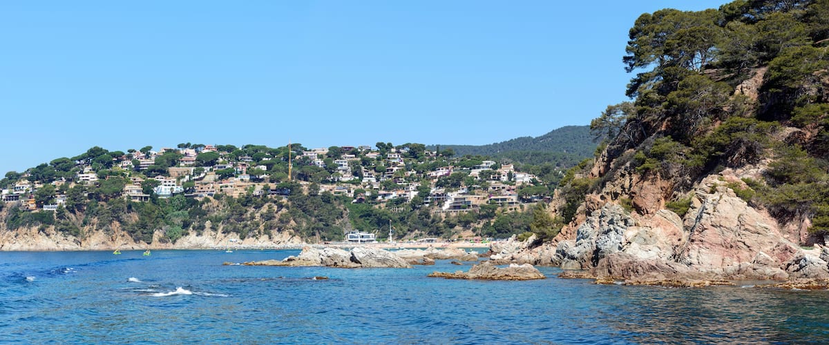A coastal town with buildings on a hillside, rocky cliffs, and calm sea.