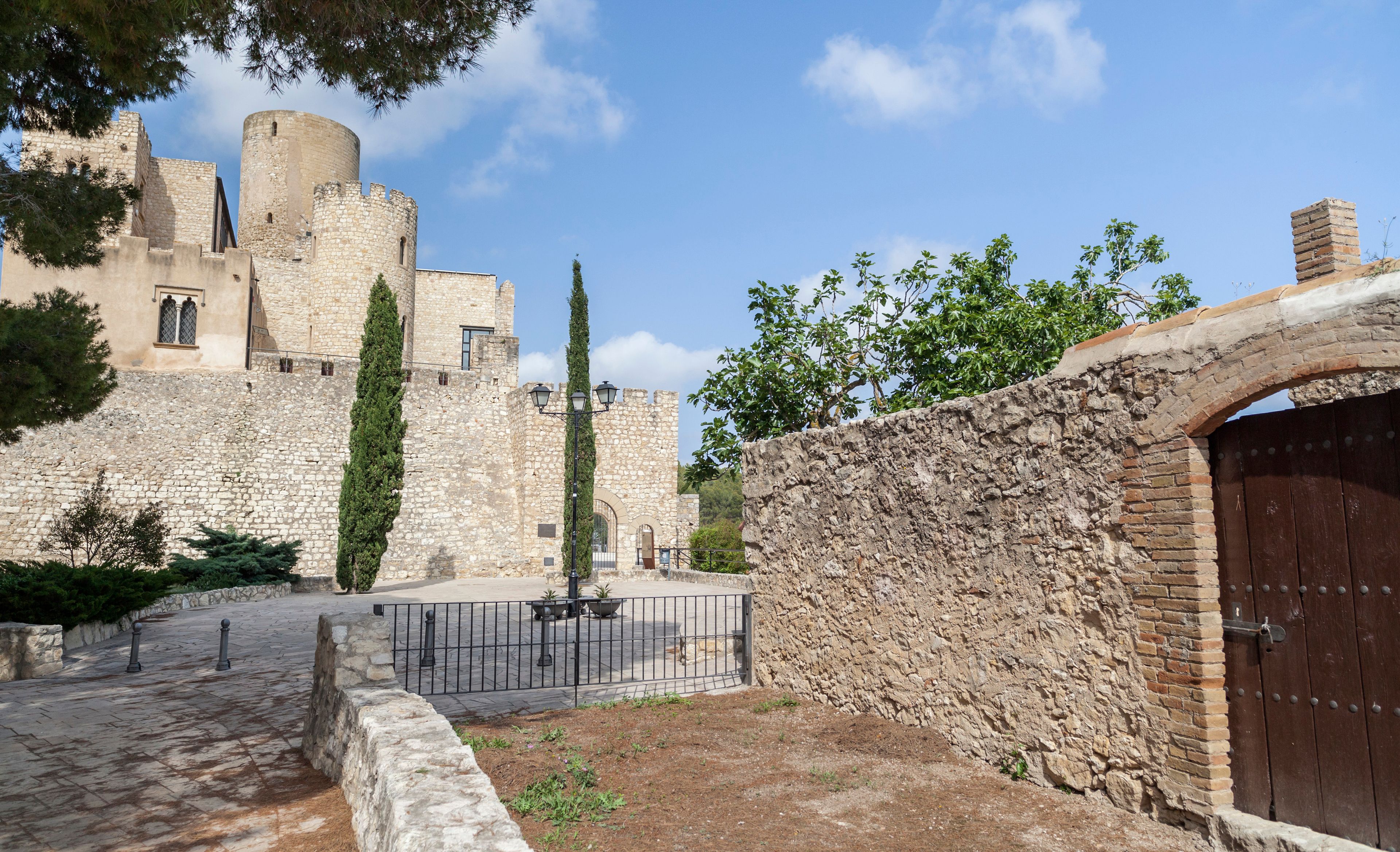 A historic stone castle with a round tower, a paved courtyard, and a wooden gate.