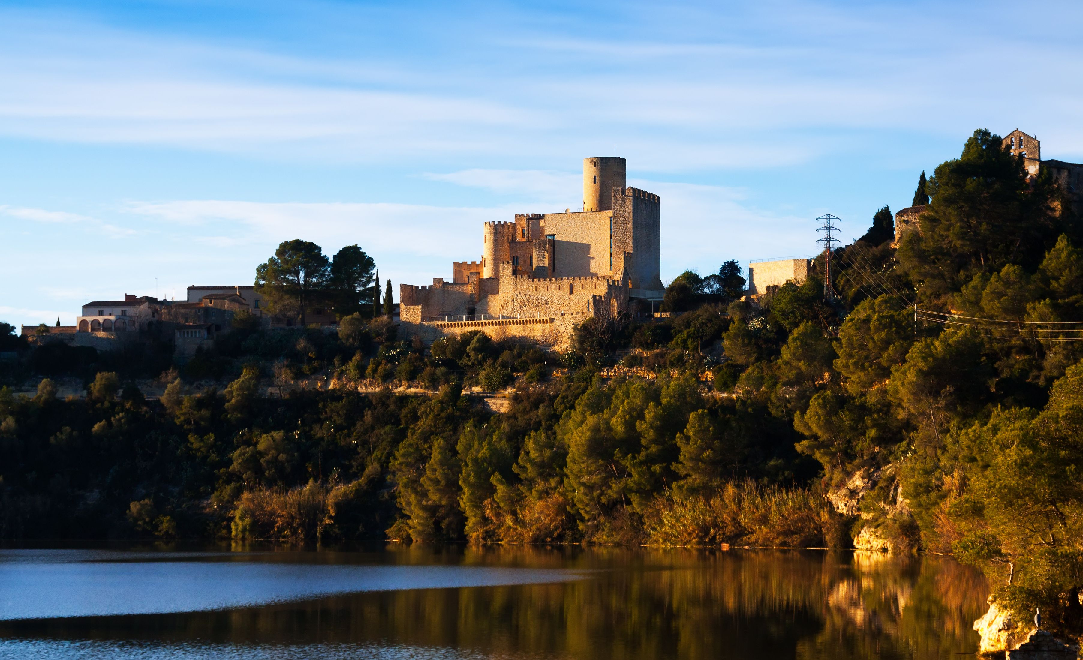 A historic castle on a hill overlooking a lake, surrounded by dense forest.