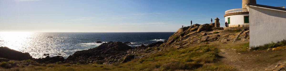 Un paysage côtier avec un phare, un terrain rocheux et l’océan.