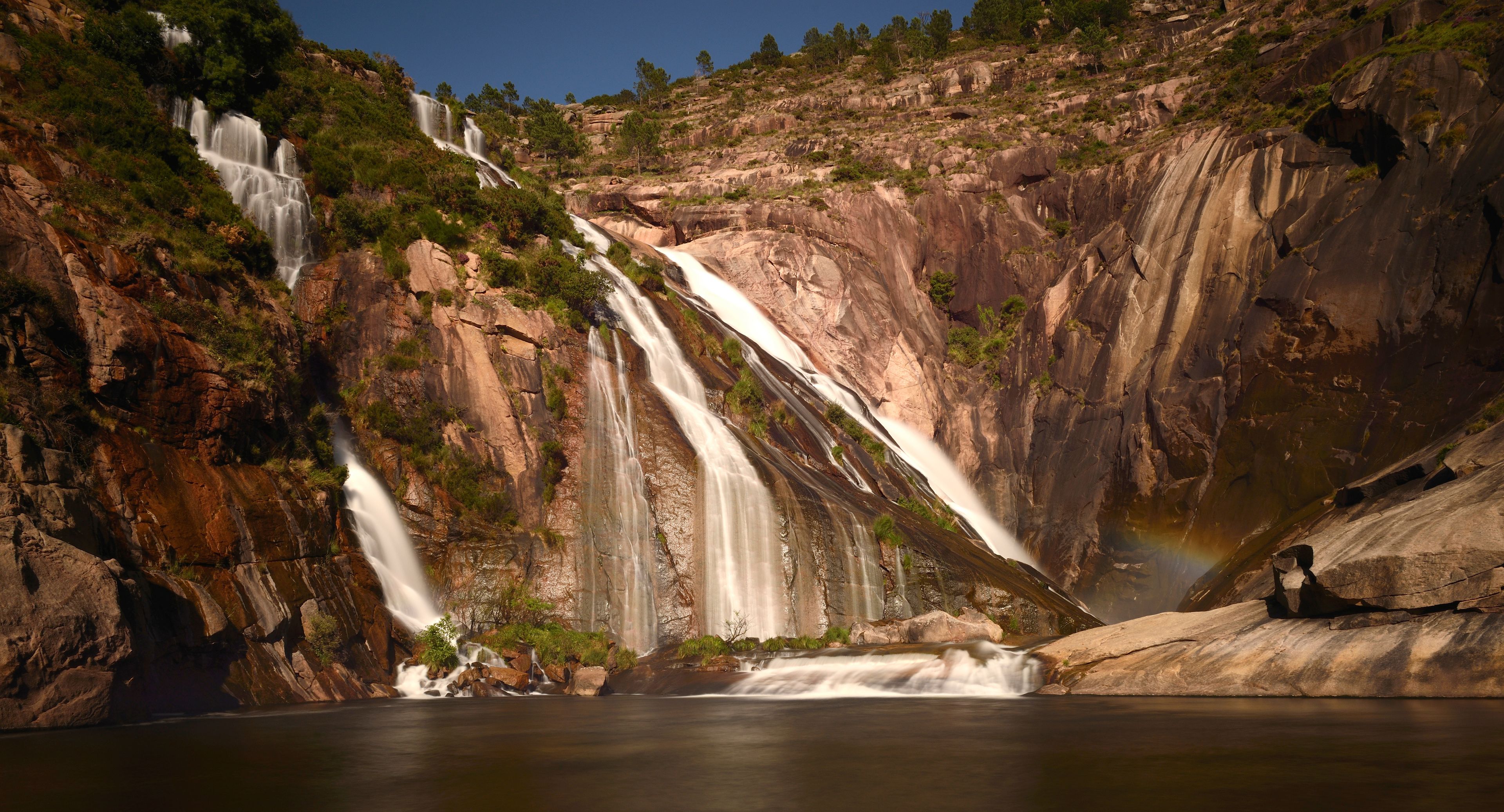 A multi-tiered waterfall cascading down a rocky cliff into a calm river.
