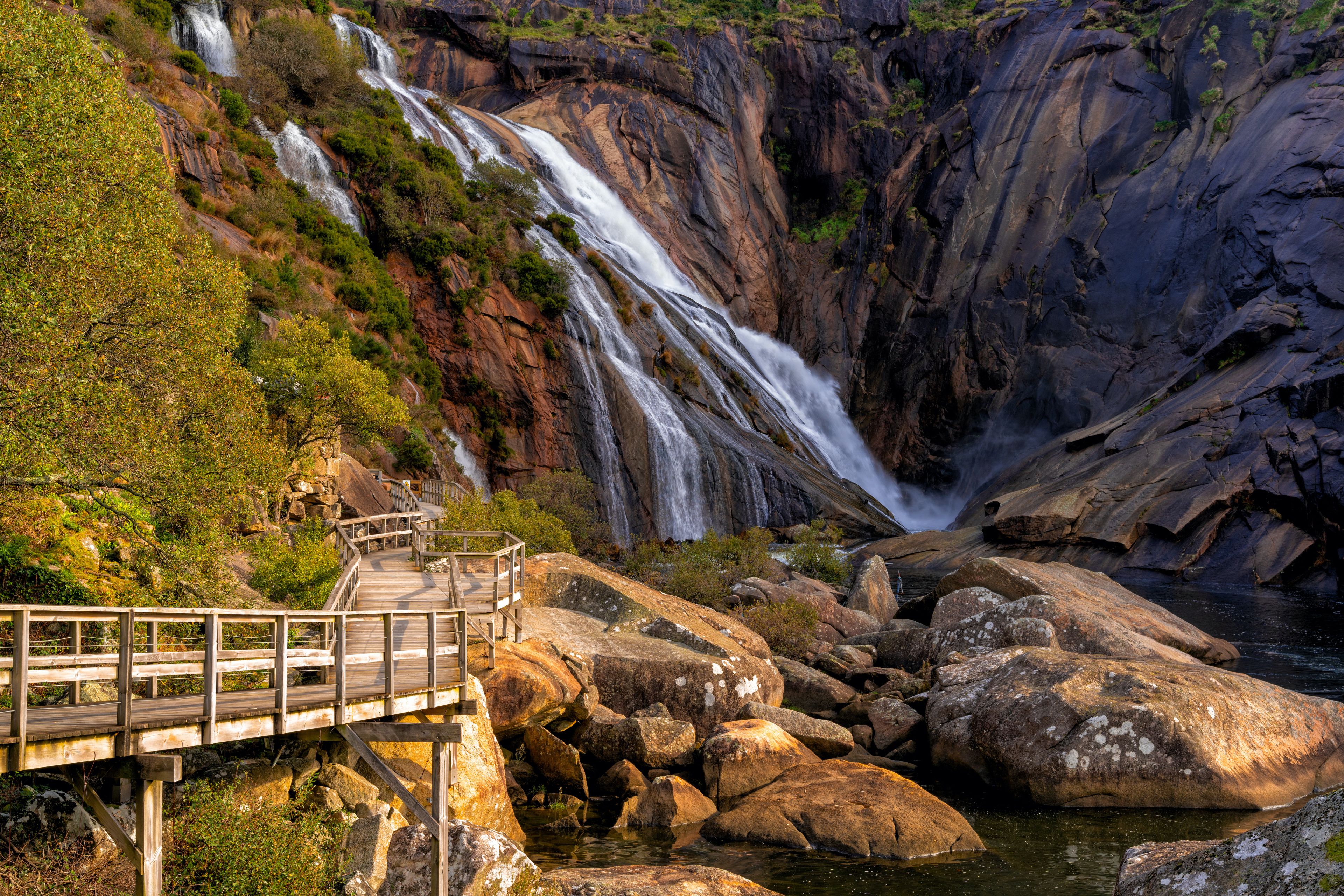 Un pont en bois menant à une cascade, entourée de gros rochers et de verdure.