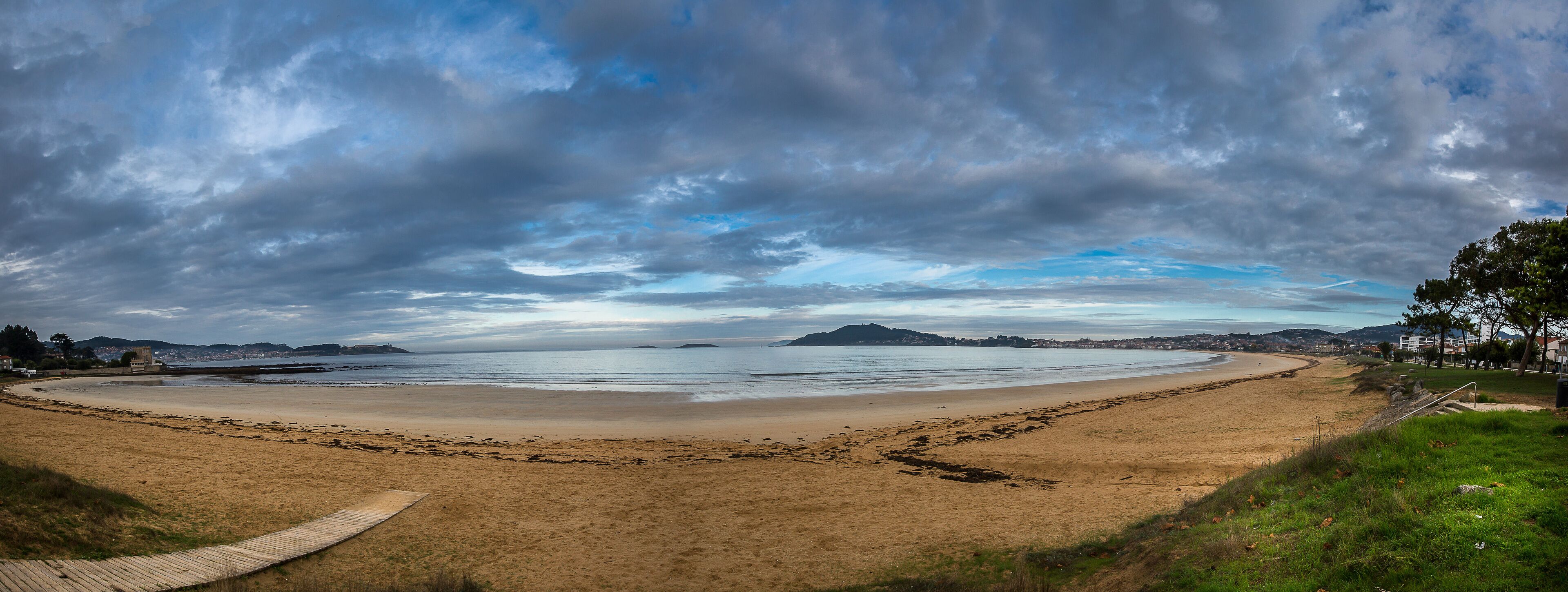 A beach with a wooden boardwalk, sandy shore, and distant hills.