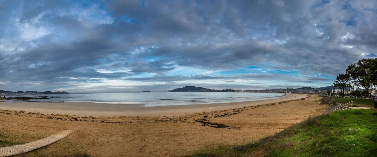 A beach with a wooden boardwalk, sandy shore, and distant hills.
