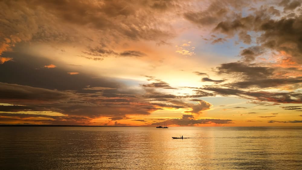 A sunset over a calm sea with a boat and a distant ship.