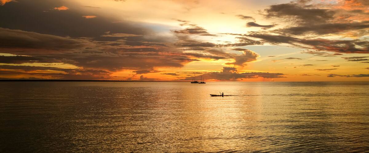 A sunset over a calm sea with a boat and a distant ship.