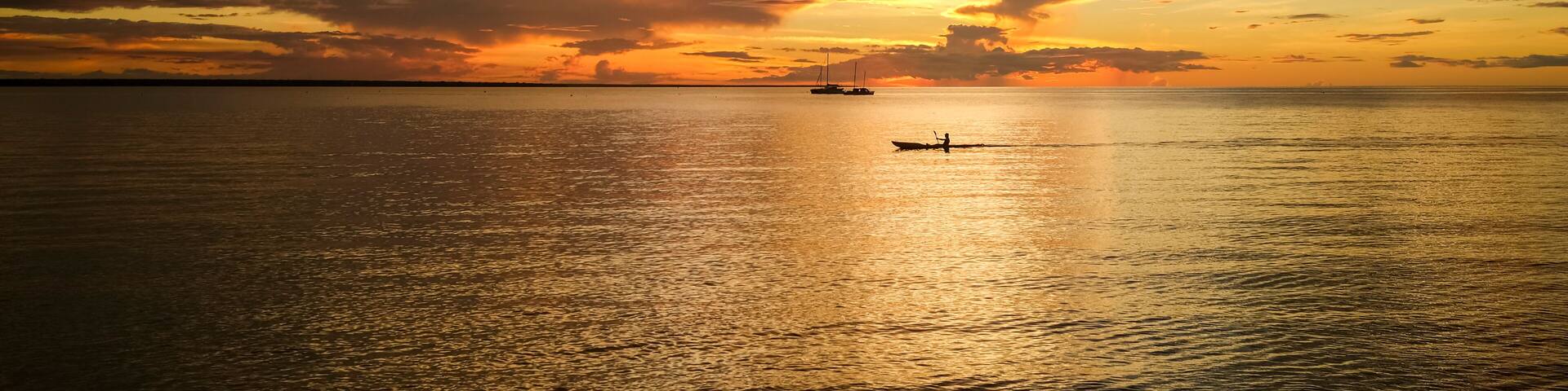 A sunset over a calm sea with a boat and a distant ship.
