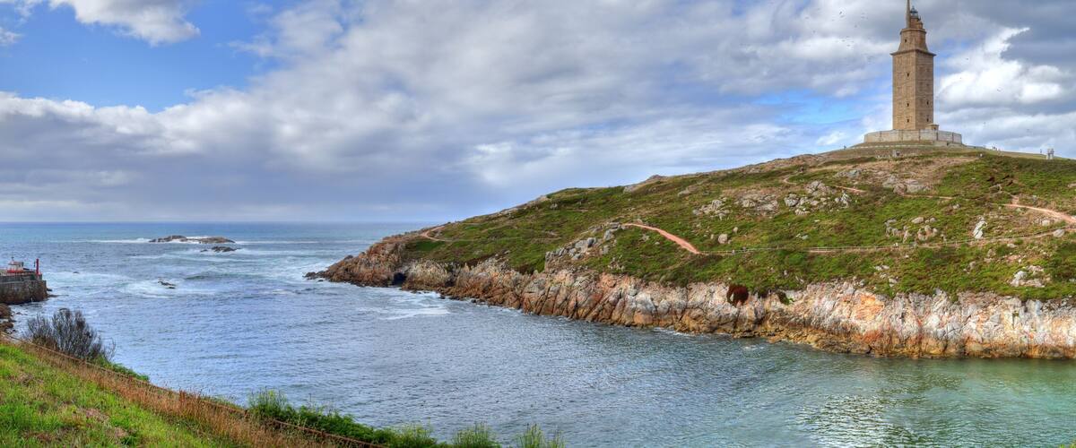 A coastal landscape with a lighthouse on a hill, rocky shoreline, and a path leading to the lighthouse.