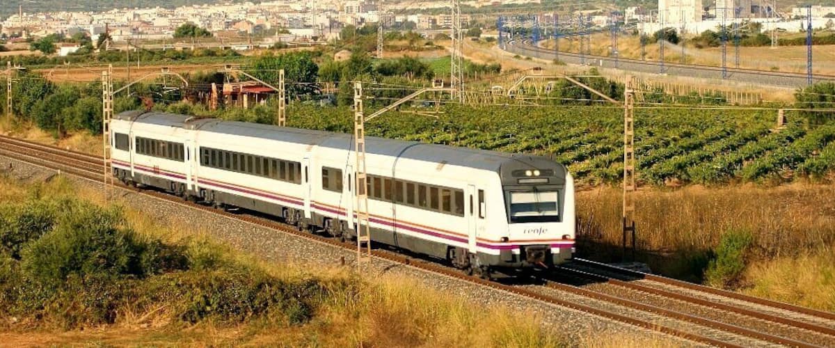 A train traveling on tracks through a rural area with fields and a distant town.