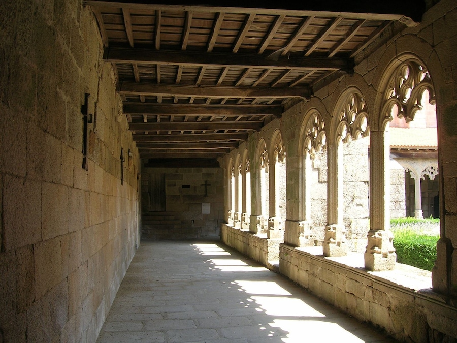 Un pasillo de piedra con vigas de madera y ventanas de arco.