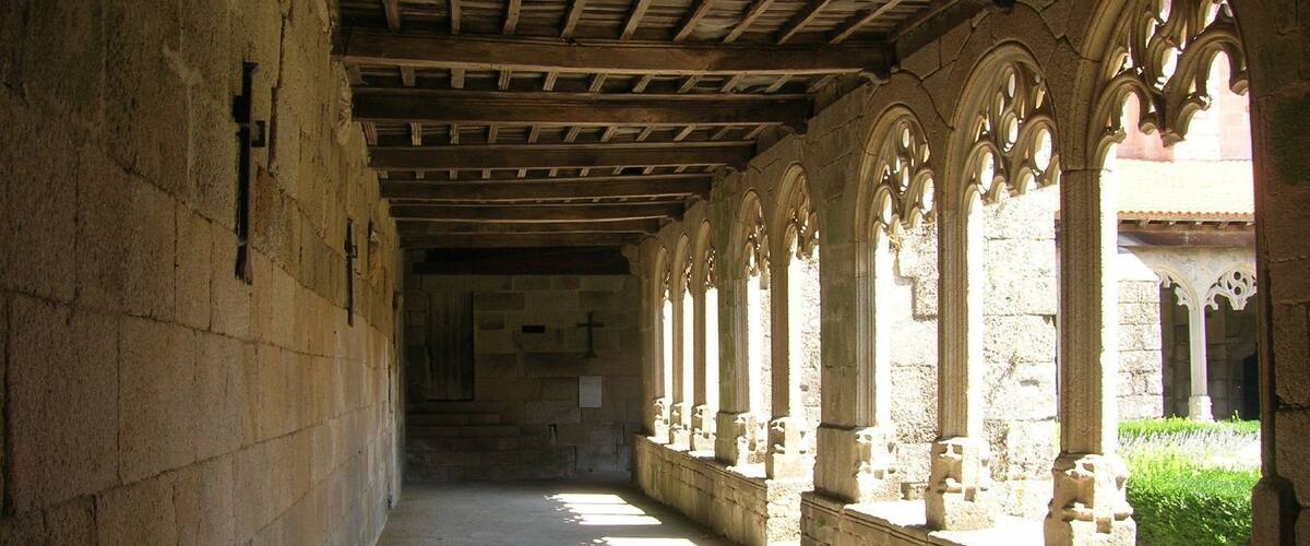 A stone corridor with wooden beams and arched windows.