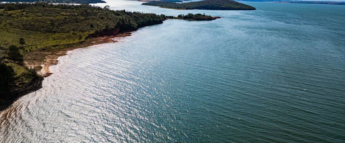 A coastal landscape with a sandy beach, a forested area, and a large body of water.