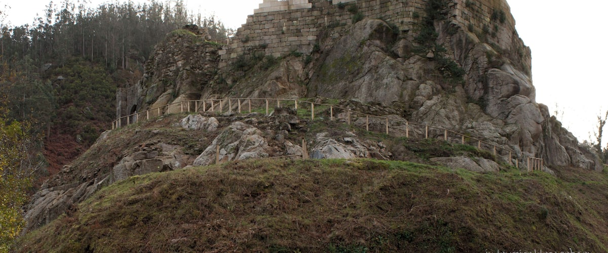 A large, ancient stone tower on a rocky hill with a forested background.