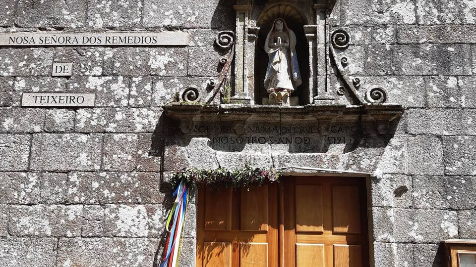 A stone building with a wooden door and a statue of a religious figure.