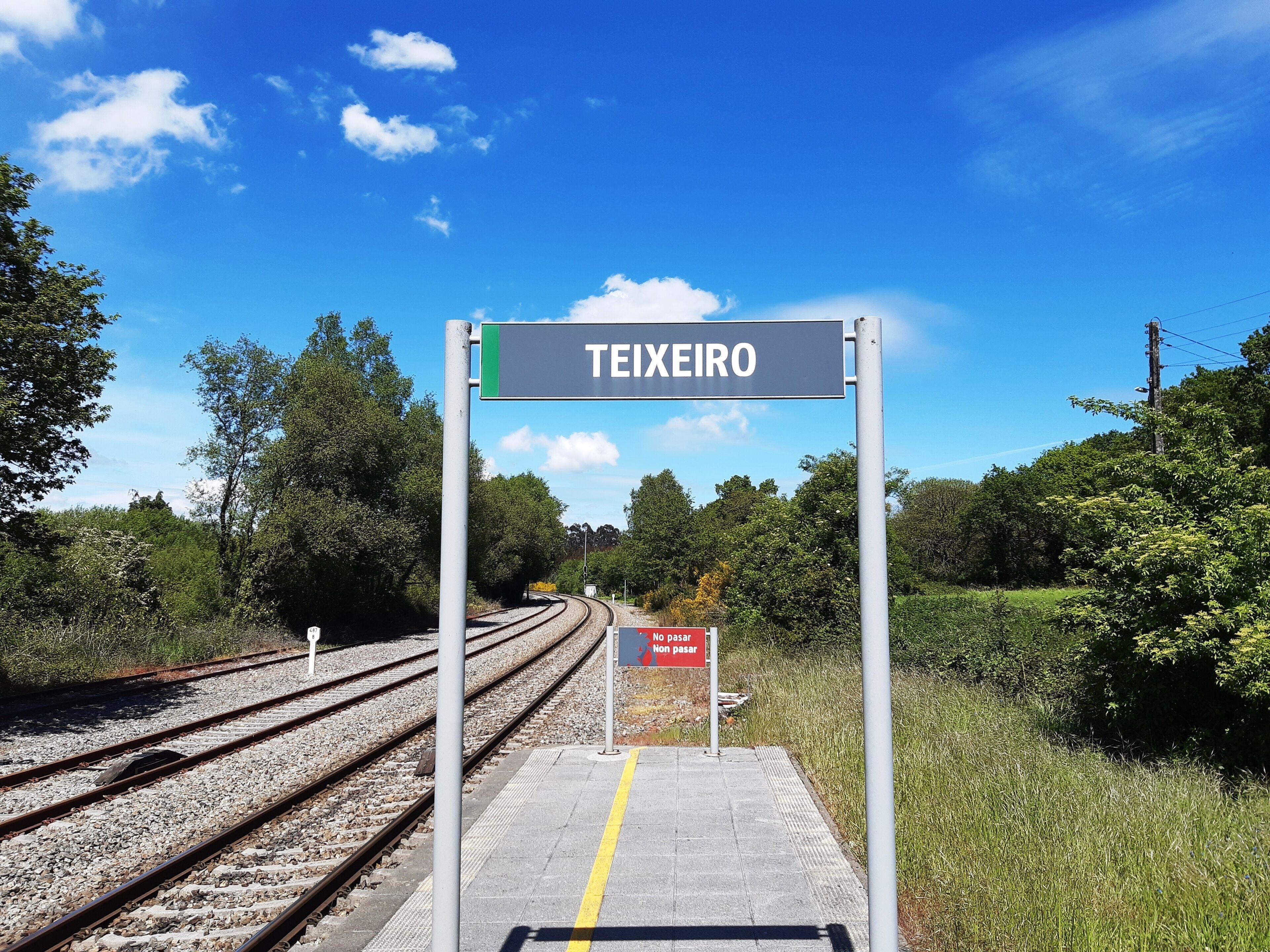 A railway station platform with a sign reading "TEIXEIRO" and a "NO PASAR" sign.