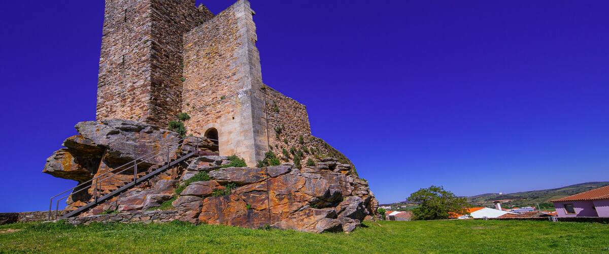 A stone tower with a staircase leading up to an arched doorway, surrounded by grass and a clear blue sky.
