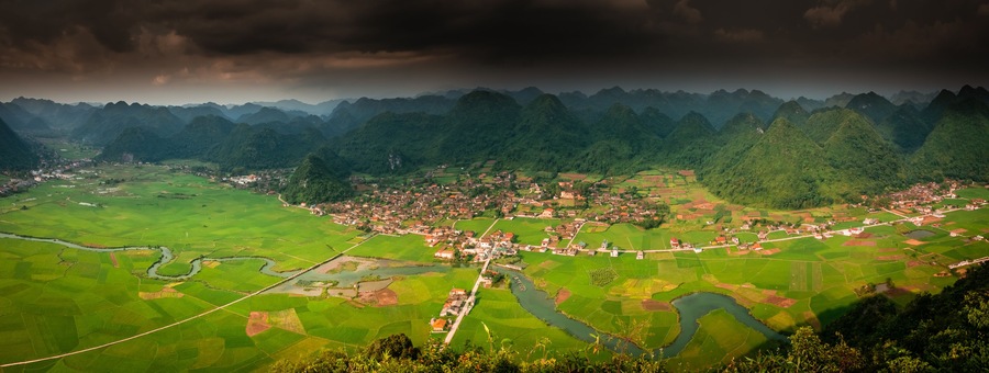 A mountainous landscape with a village nestled among terraced fields and a river.