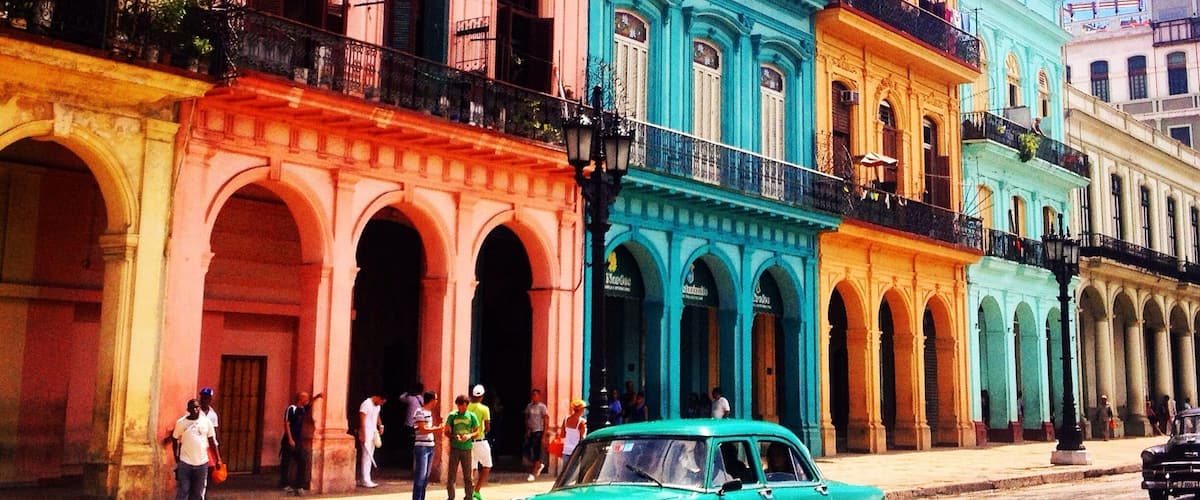 A colorful street with pastel-colored buildings and a vintage green car parked on the side.