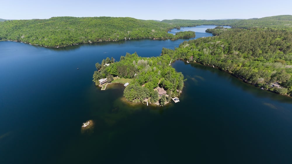 An aerial view of a lake surrounded by dense forest and a small island with buildings.
