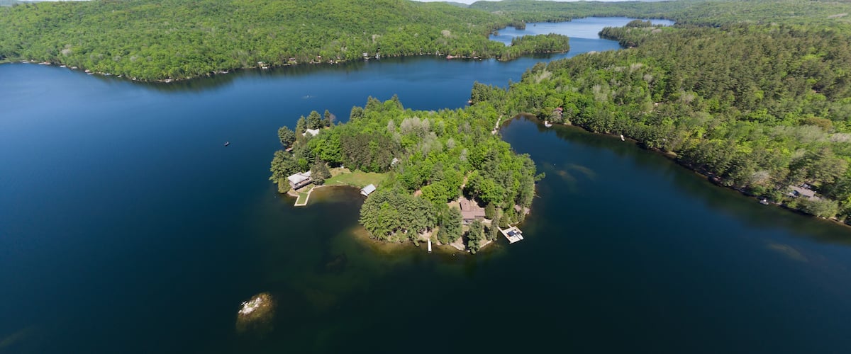 Une vue aérienne d’un lac entouré d’une forêt dense et d’une petite île où se trouvent des bâtiments.