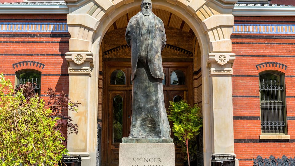 A statue in front of a red brick building with arched windows and decorative elements.