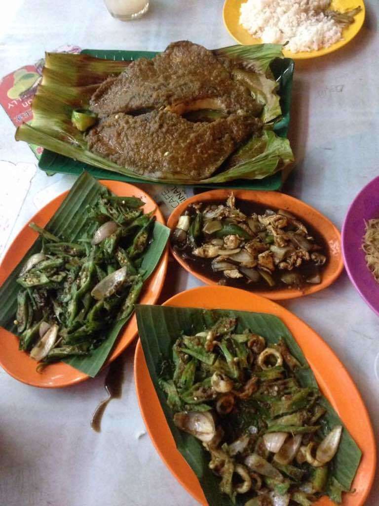 A variety of dishes served on banana leaves, including fried fish, stir-fried vegetables, and a plate of rice.