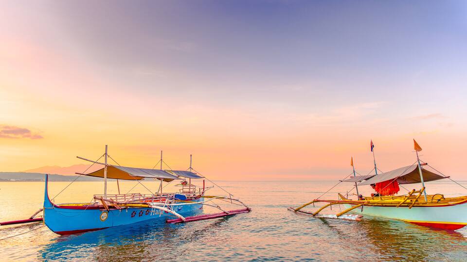 Two traditional boats anchored at sunset on calm waters with a clear sky.