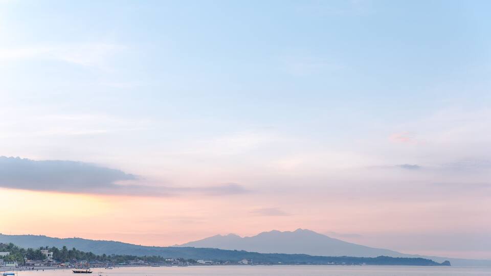 A calm sea with boats, a distant mountain range, and a clear sky.
