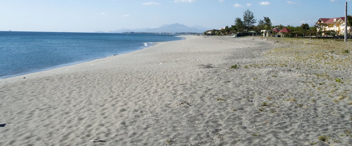 A sandy beach with a clear blue sky and distant mountains.