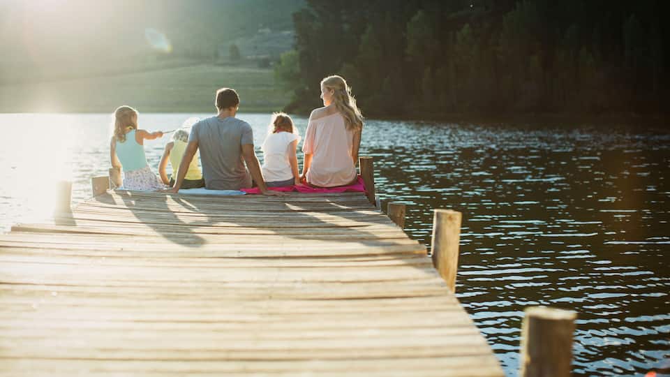 A wooden pier extending into a calm lake with a family sitting at the end.