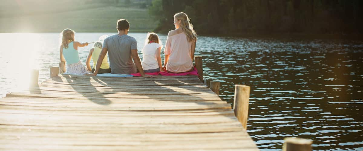 A wooden pier extending into a calm lake with a family sitting at the end.