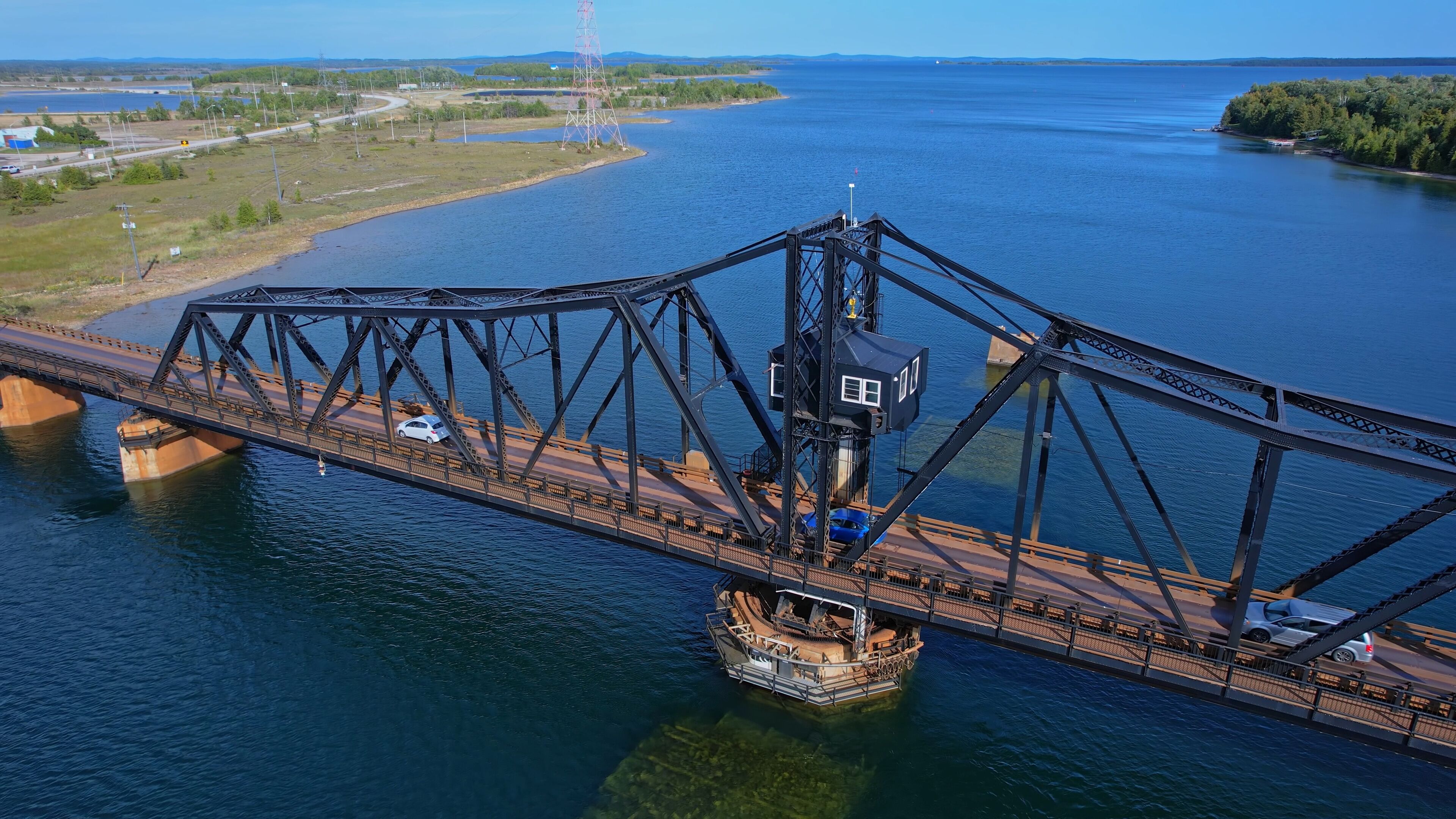 A large steel bridge spanning a wide river with a boat docked on the right side.