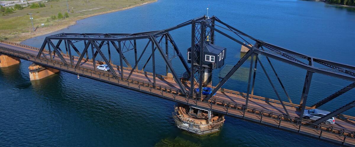 A large steel bridge spanning a wide river with a boat docked on the right side.